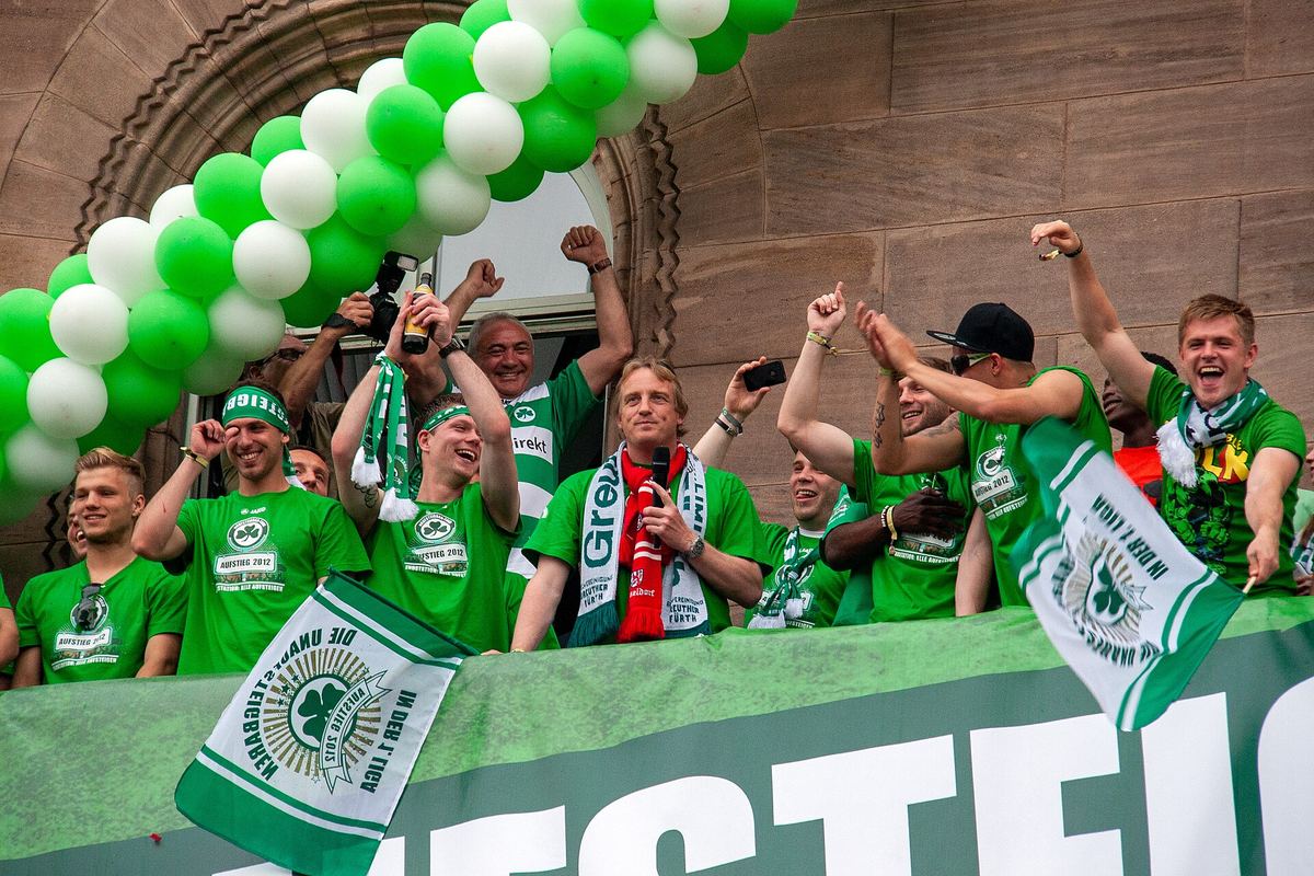 Spieler in grünen Aufstiegs-Shirts feiern auf dem Balkon des Fürther Rathauses